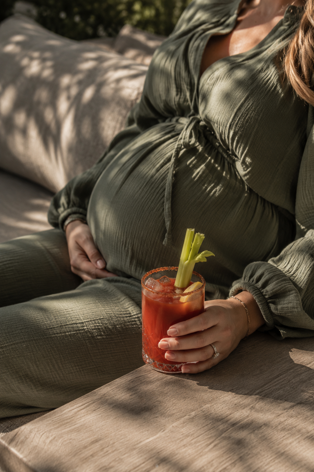 Zwangere vrouw houdt een alcoholvrije bloody mary met selderijstengel vast op een zonnig terras